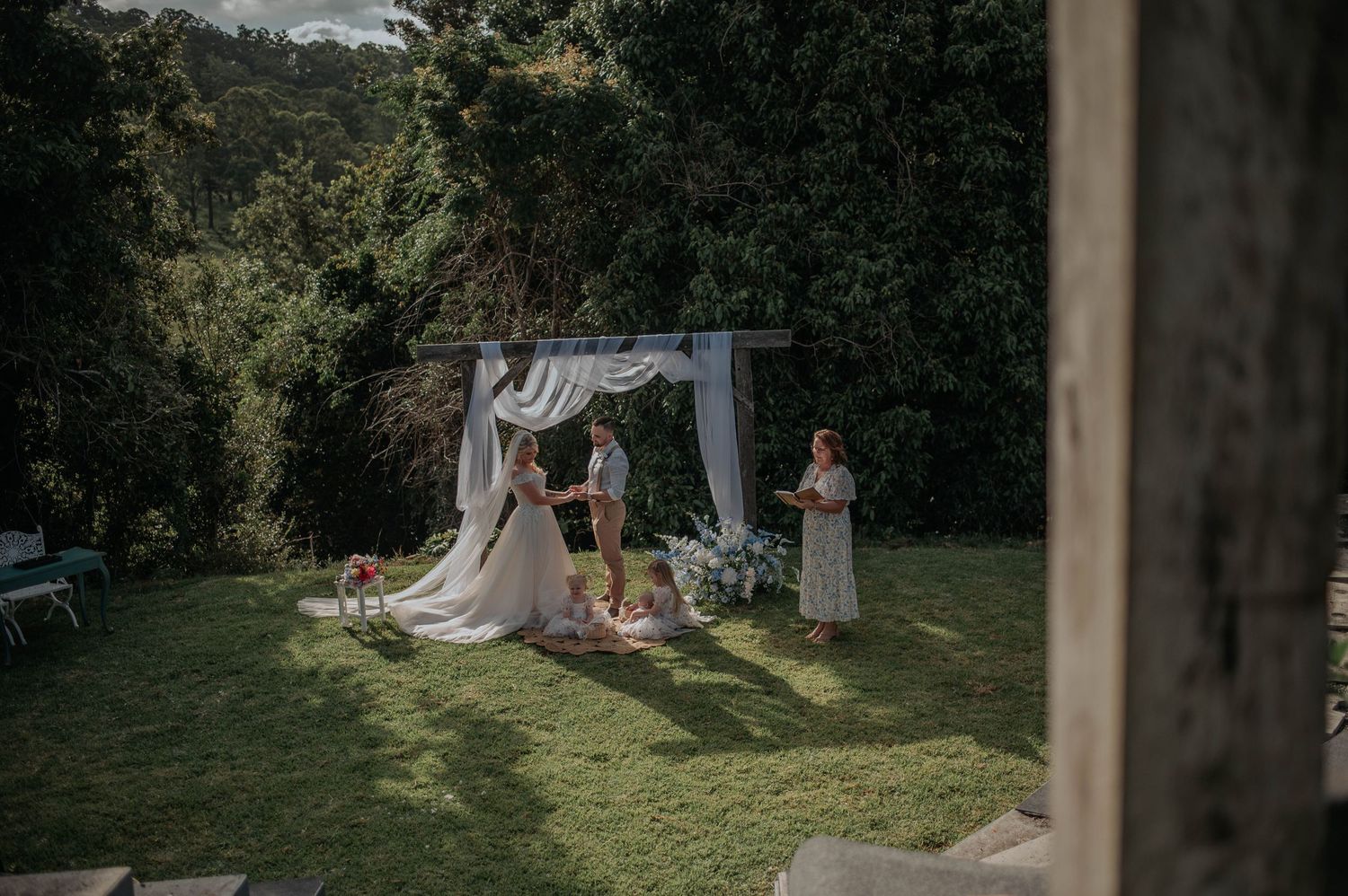A wedding ceremony in progress on a grassy hillside with white fabric decorations.