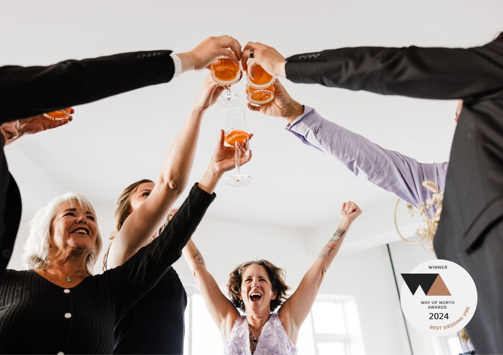 People raising glasses of beer in celebration with arms extended upward while cheering together.