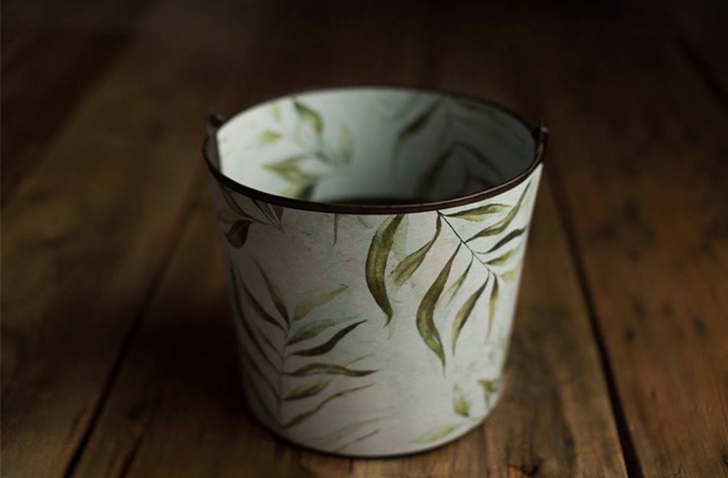 White ceramic pot with green leaf botanical print on wood table.