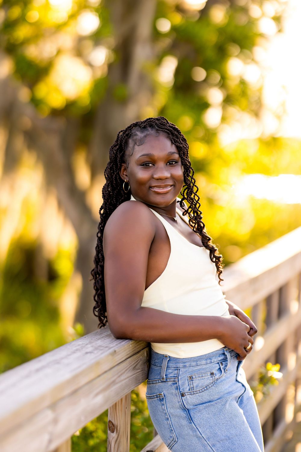 A casual portrait in white top and jeans leaning against wooden railing at sunset.