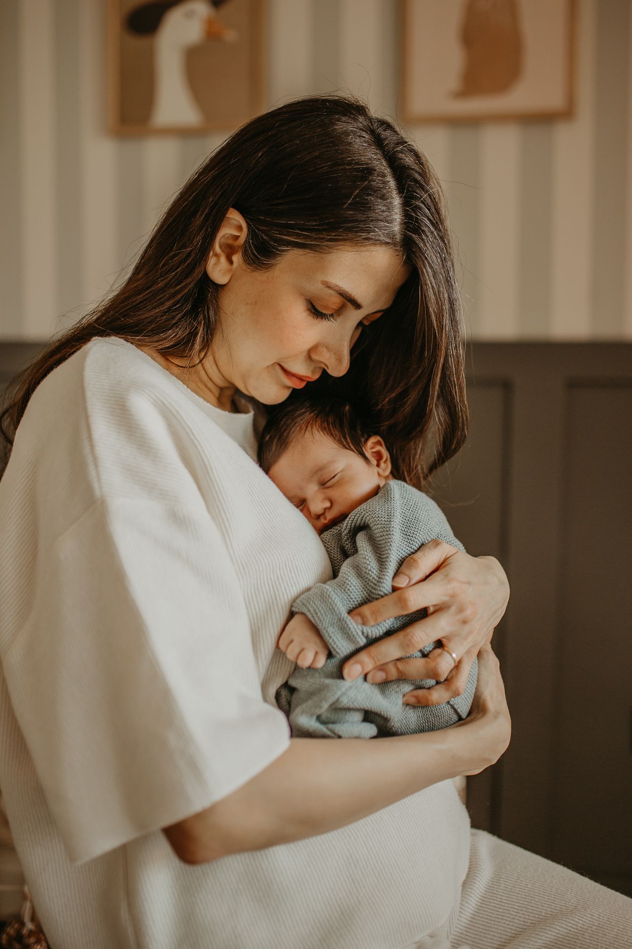 A parent wearing white cradles a sleeping newborn baby dressed in gray in a warm, intimate indoor setting.