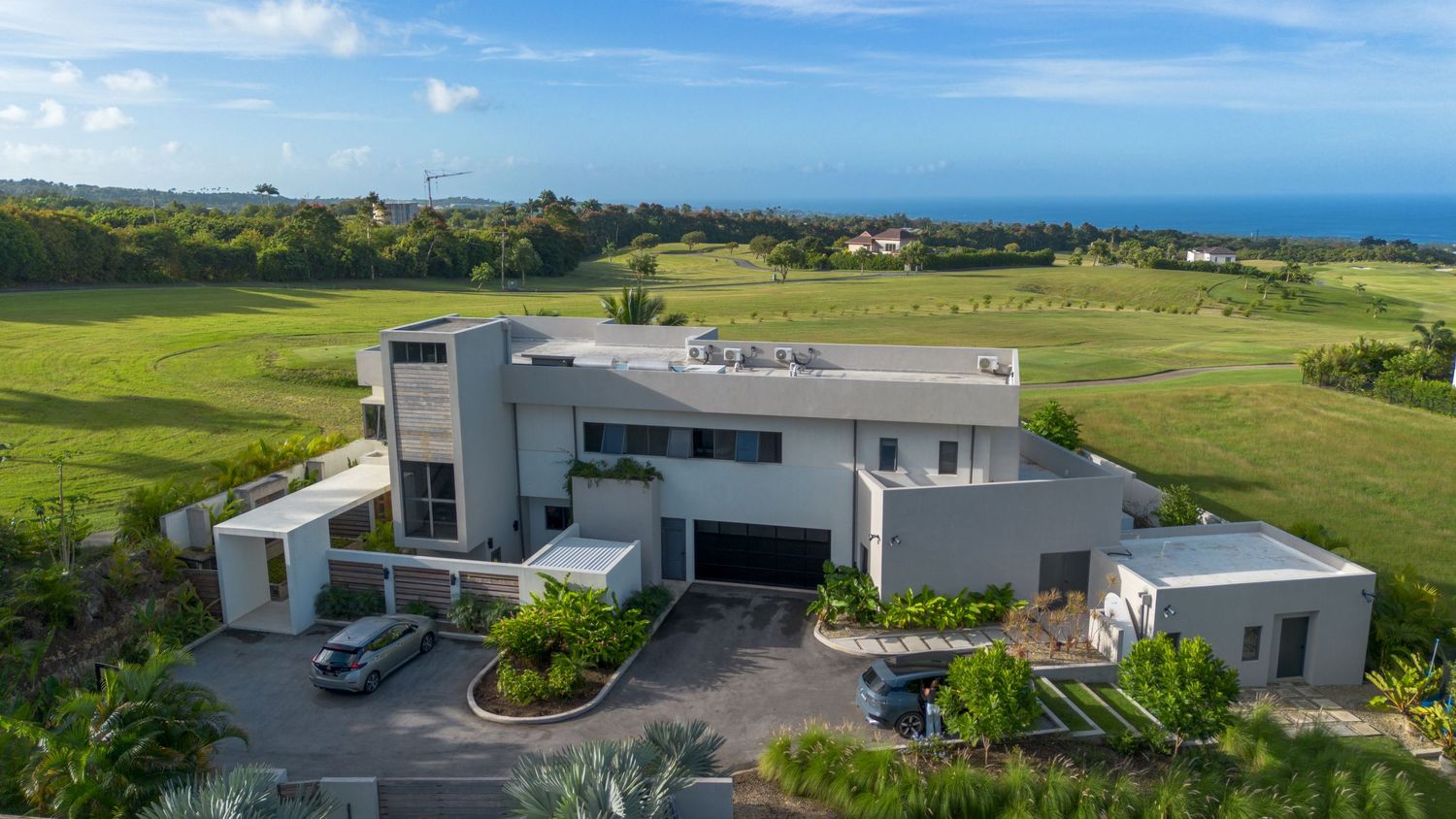 Luxurious modern mansion with white angular architecture perched on a hilltop overlooking coastal golf course and ocean views.