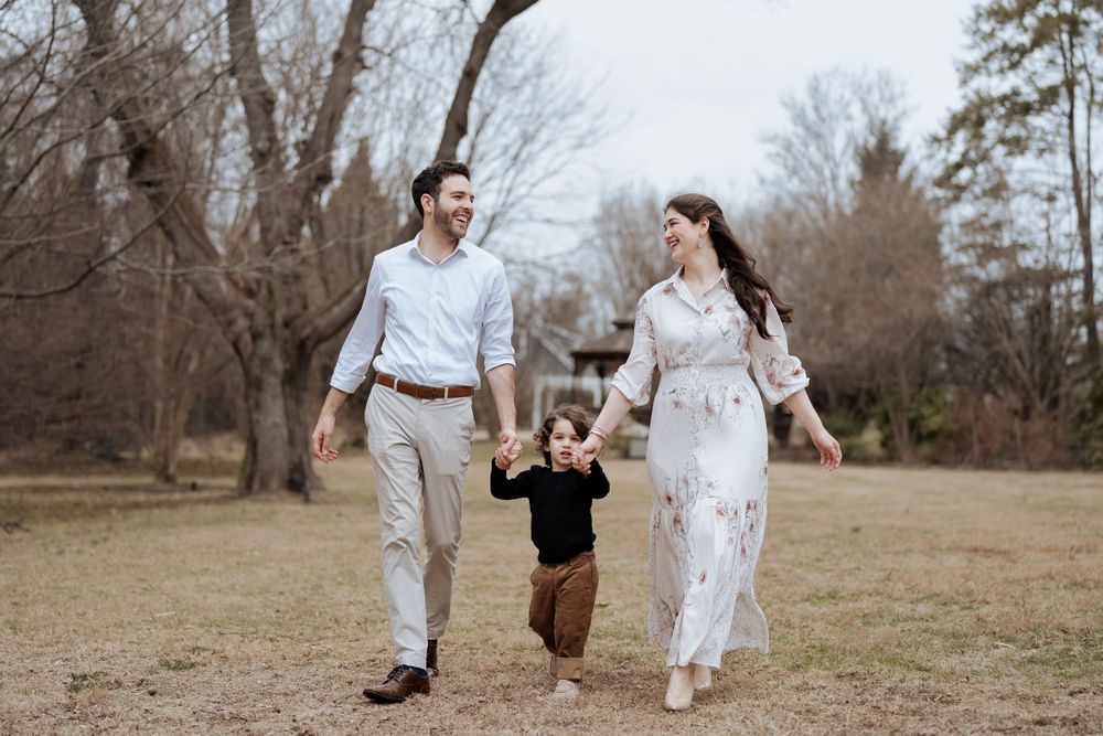 A couple walks hand-in-hand with their small child through a field on an autumn day.
