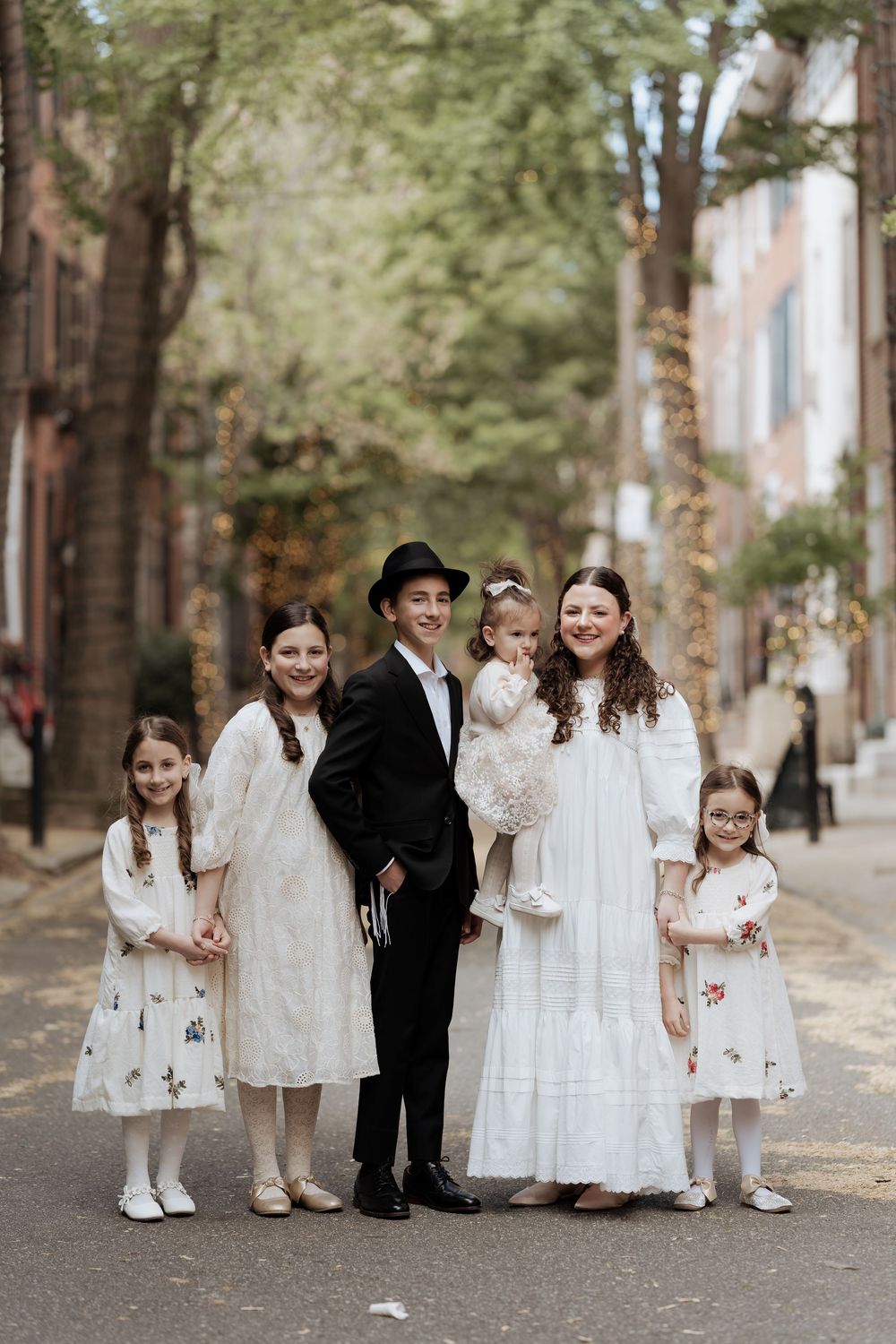Jewish family dressed in traditional clothing stands together on a tree-lined city street.