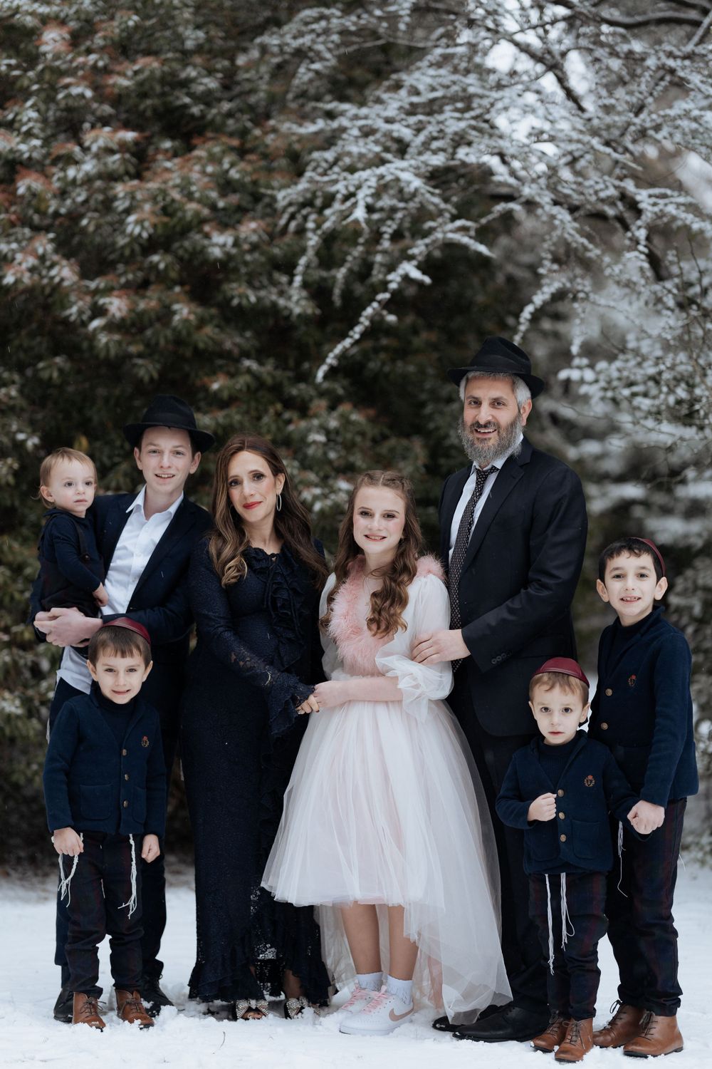 A formal family portrait in winter with snow-covered evergreens in the background.
