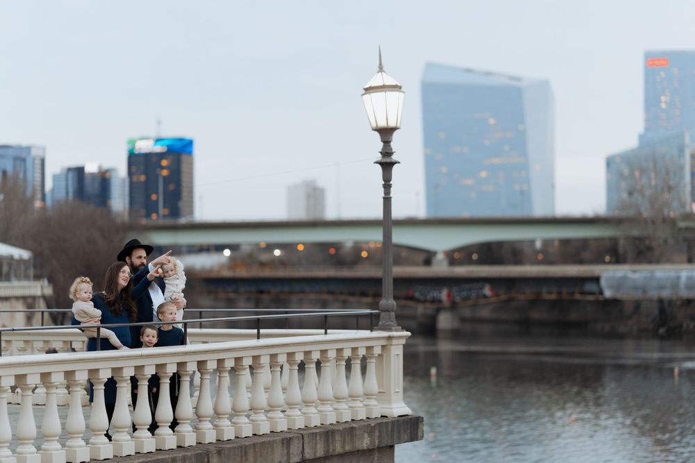 A couple sits on a stone balustrade overlooking a city waterfront with skyscrapers in the background.