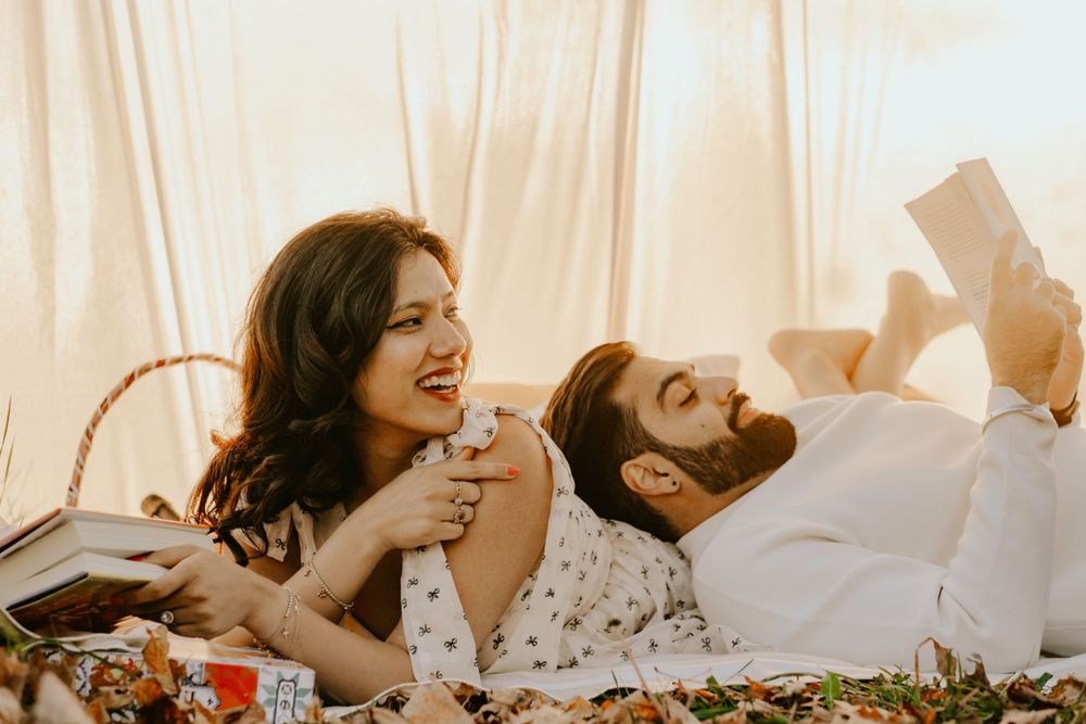 A couple laughs while having a romantic picnic outdoors on a sunny afternoon.