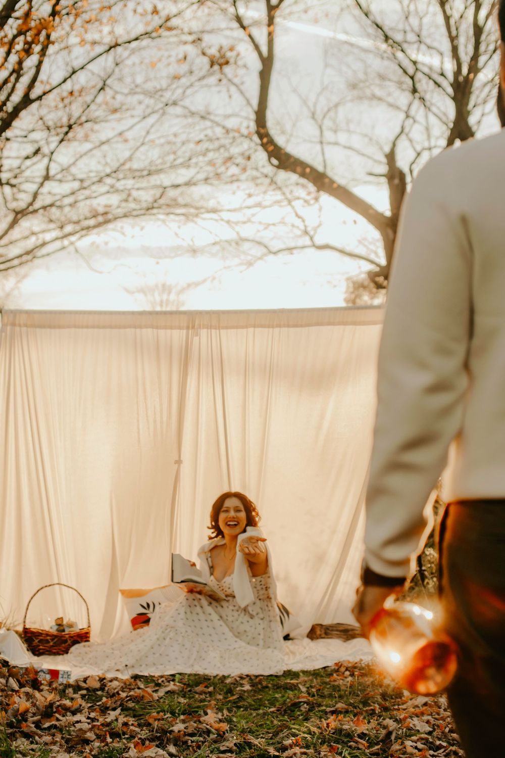 A romantic outdoor picnic setup with white drapes and fall scenery in warm sunlight.