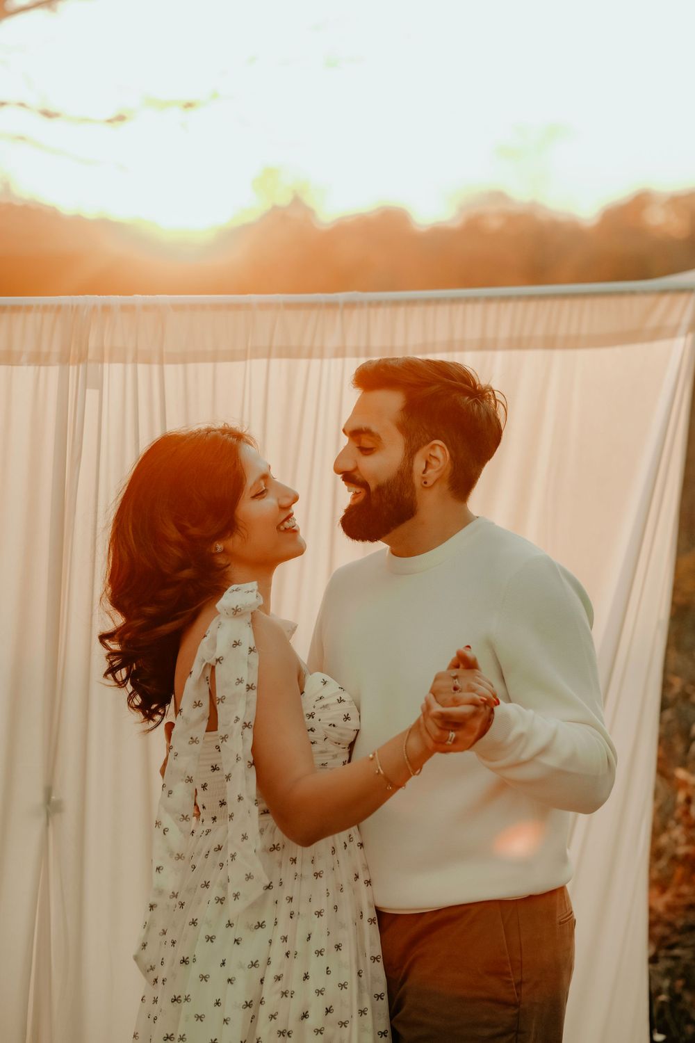 A couple dancing together against a white backdrop during golden hour in a romantic outdoor photoshoot.