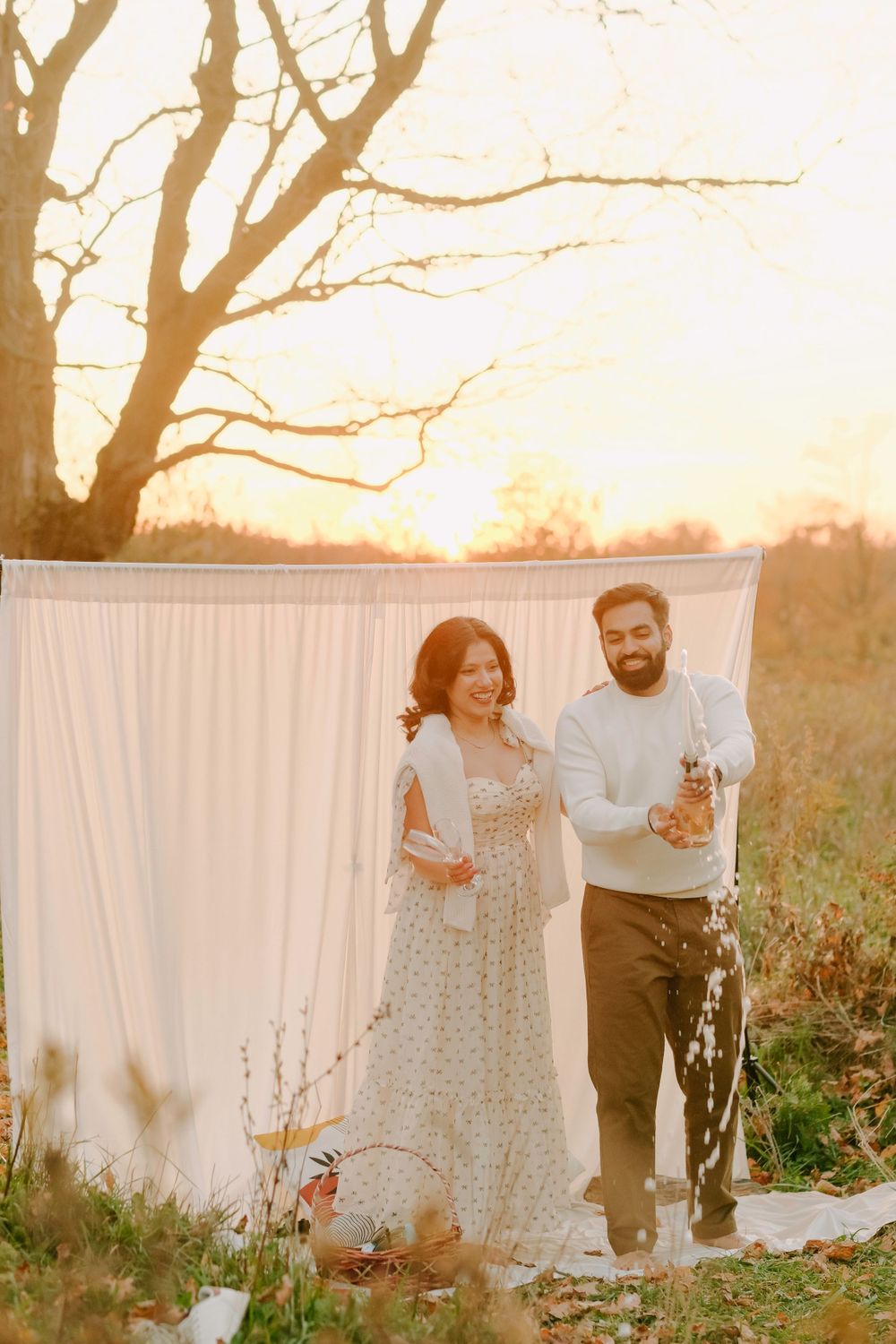 A couple sharing laughter together in front of a white backdrop during sunset in a natural outdoor setting.