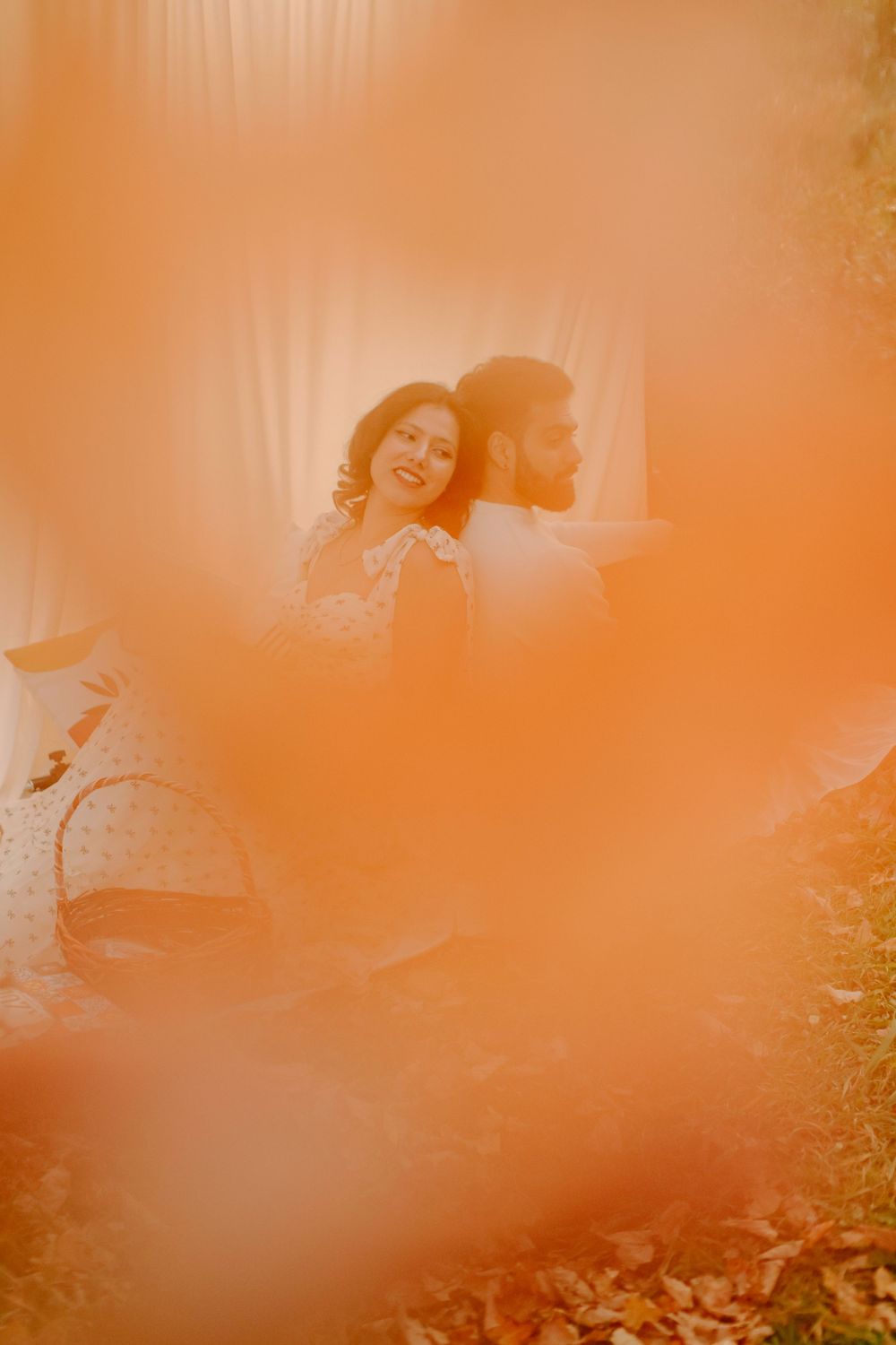 An artistic orange-tinted photo of a couple standing together against a white backdrop outdoors.