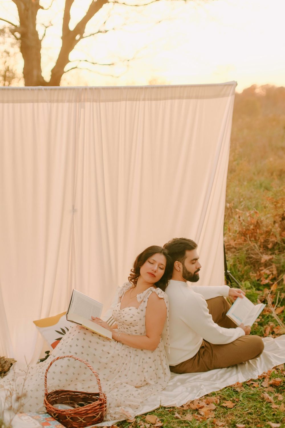 Couple reading books while relaxing on picnic blanket against white backdrop at sunset.