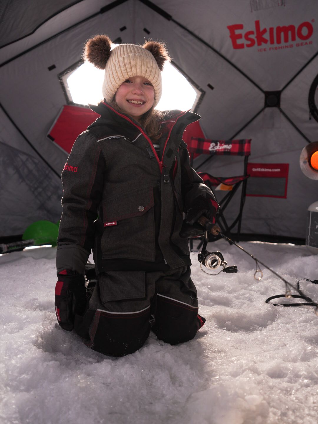 Winter ice fishing scene inside a red Eskimo shelter with people sitting on the snowy surface.