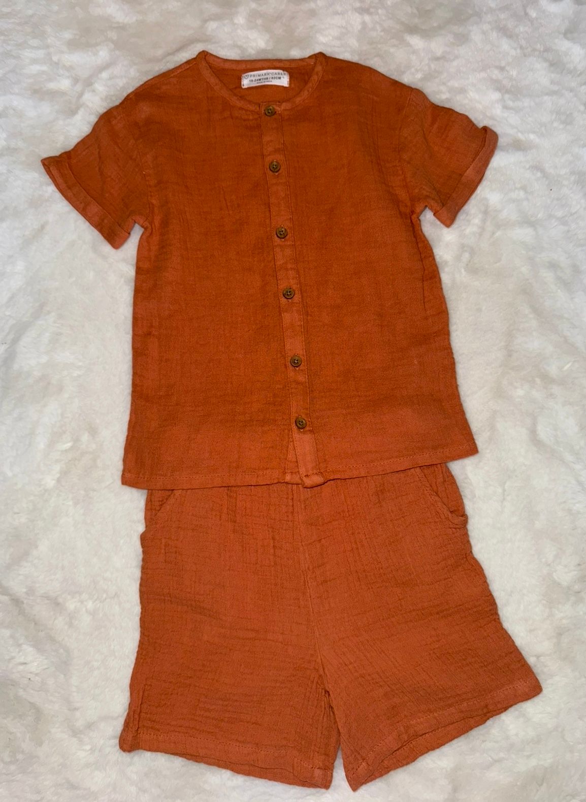 Rust-colored linen two-piece baby outfit with button-front shirt and matching shorts.