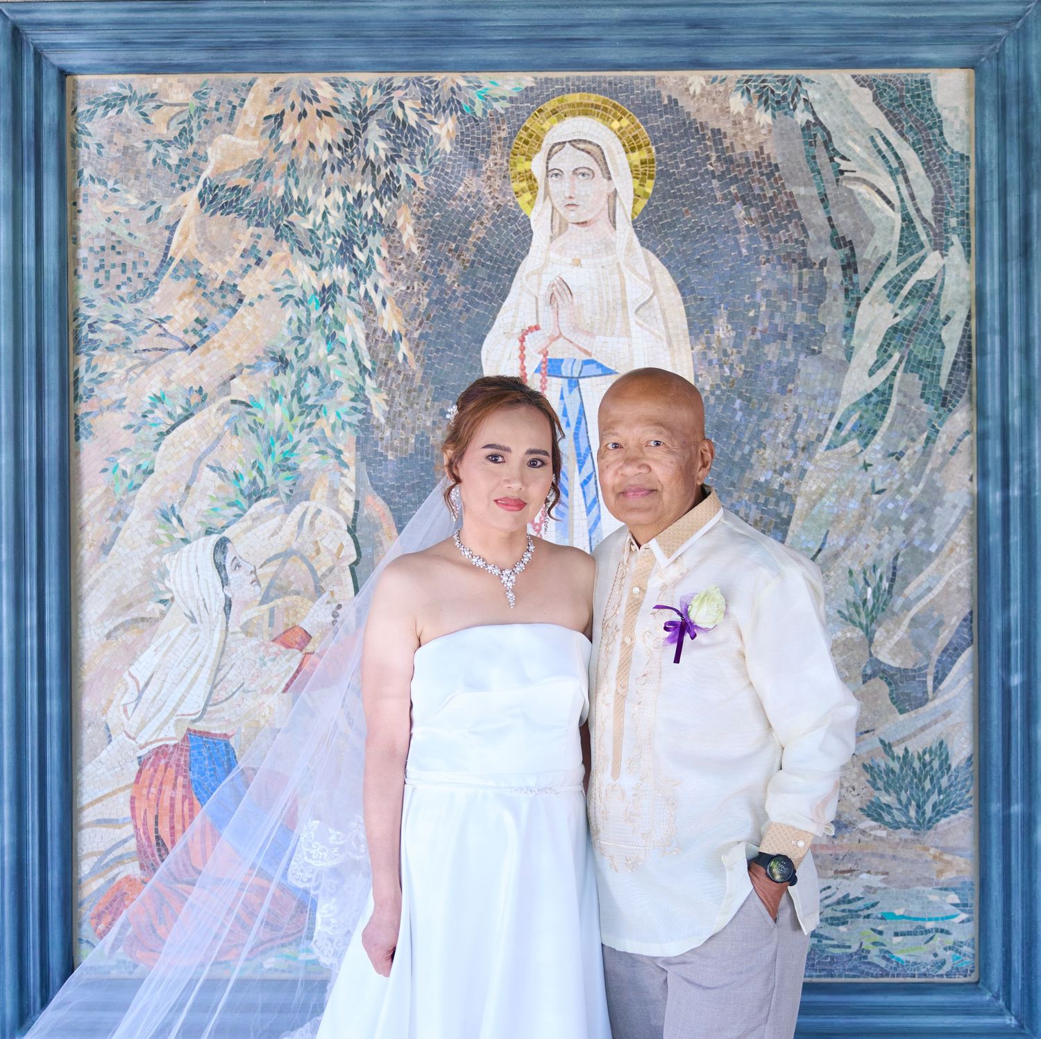 A romantic wedding moment captured outdoors with a white bridal gown, beige suit and natural greenery in the background.