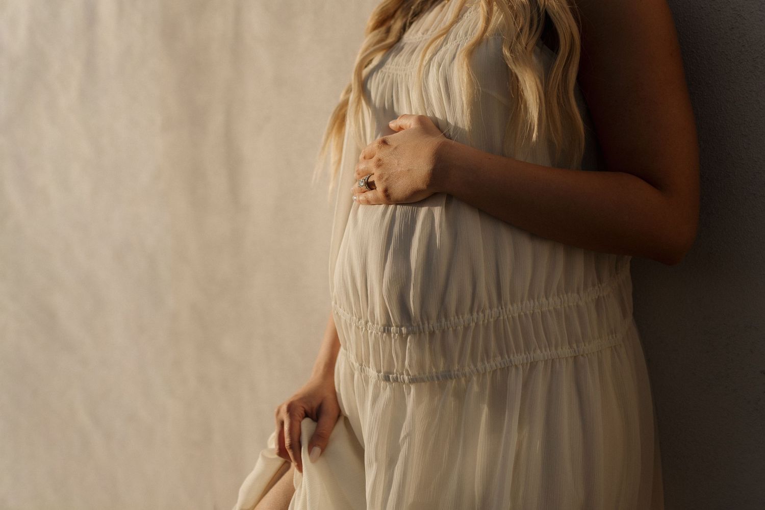 A close-up of hands cradling a pregnant belly while wearing casual denim and white clothing.