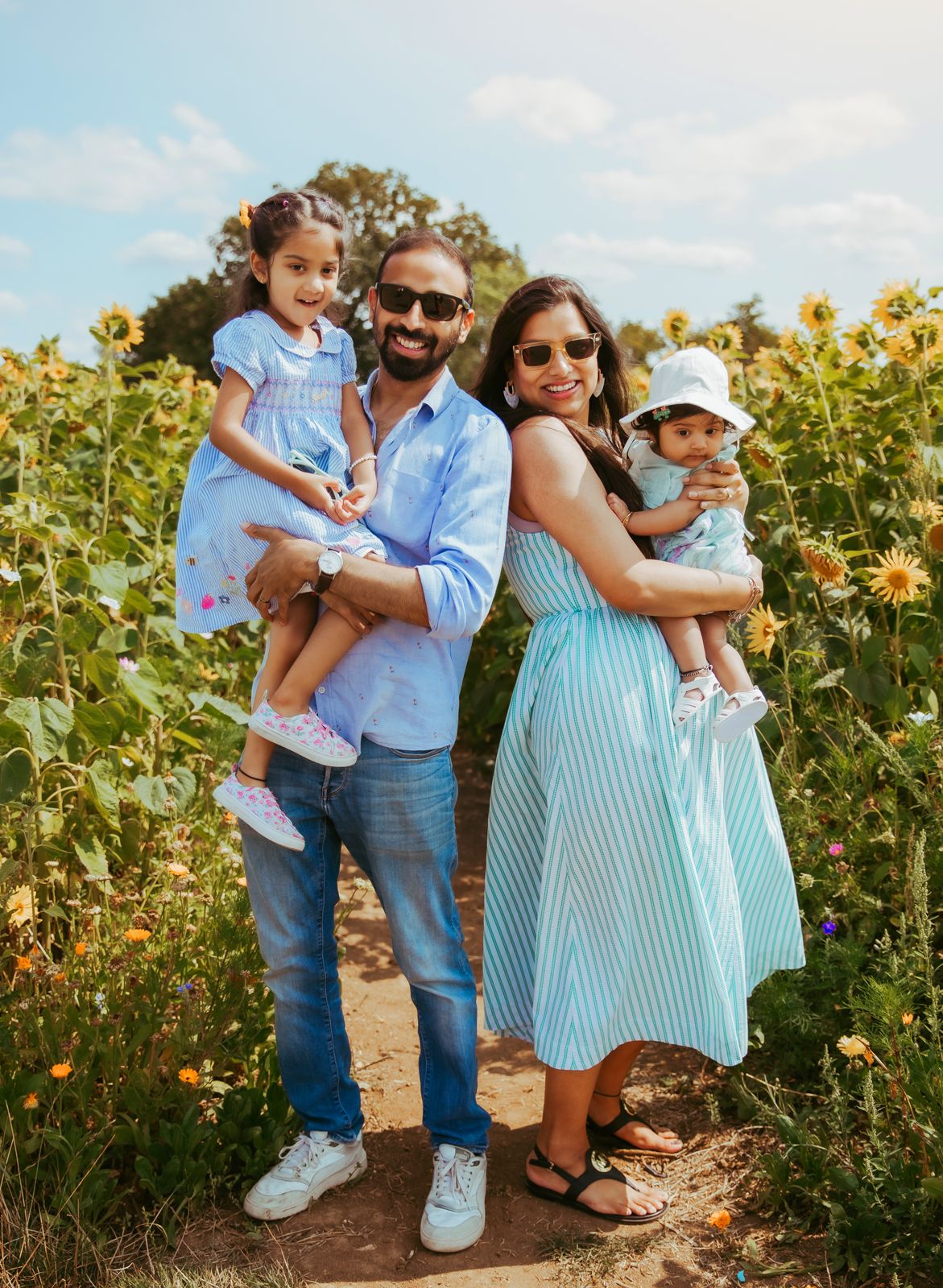Family enjoying a sunny day together in a vibrant sunflower field wearing blue and white summer outfits. During a photoshoot in London