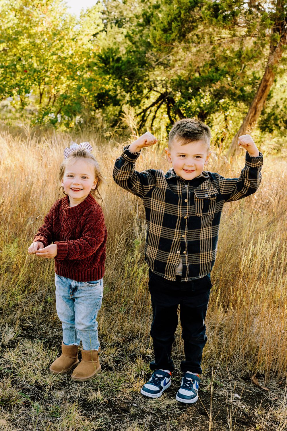 Two young children playing and laughing together in a golden autumn field with tall grass and trees in background.