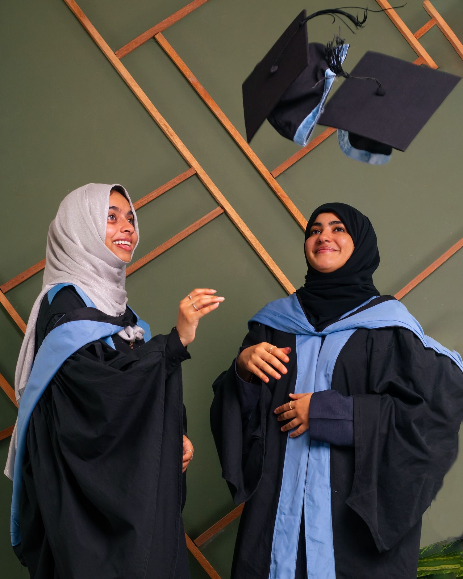 Two ladies with gowns happy throwing graduation caps to the air