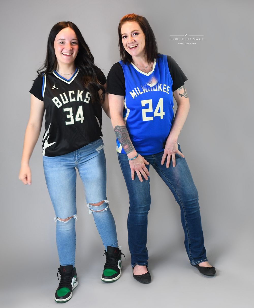 Two sports fans wearing Milwaukee Bucks jerseys pose together in a studio setting.