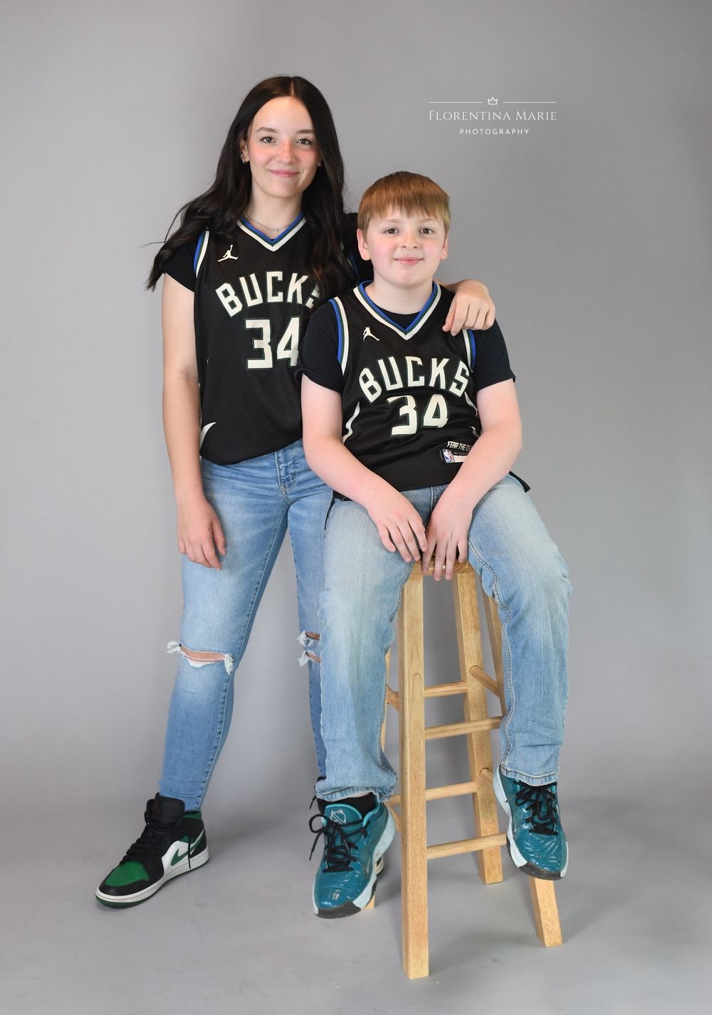 Two people in Bucks jerseys posing with wooden stool in studio setting.