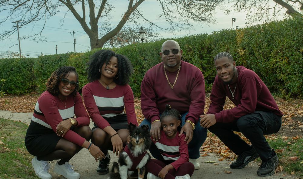 Family sitting together with pet dog wearing matching burgundy and white striped outfits.