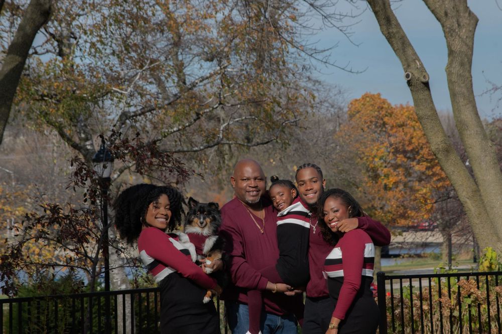 Family portrait outdoors with autumn trees and burgundy coordinated outfits.