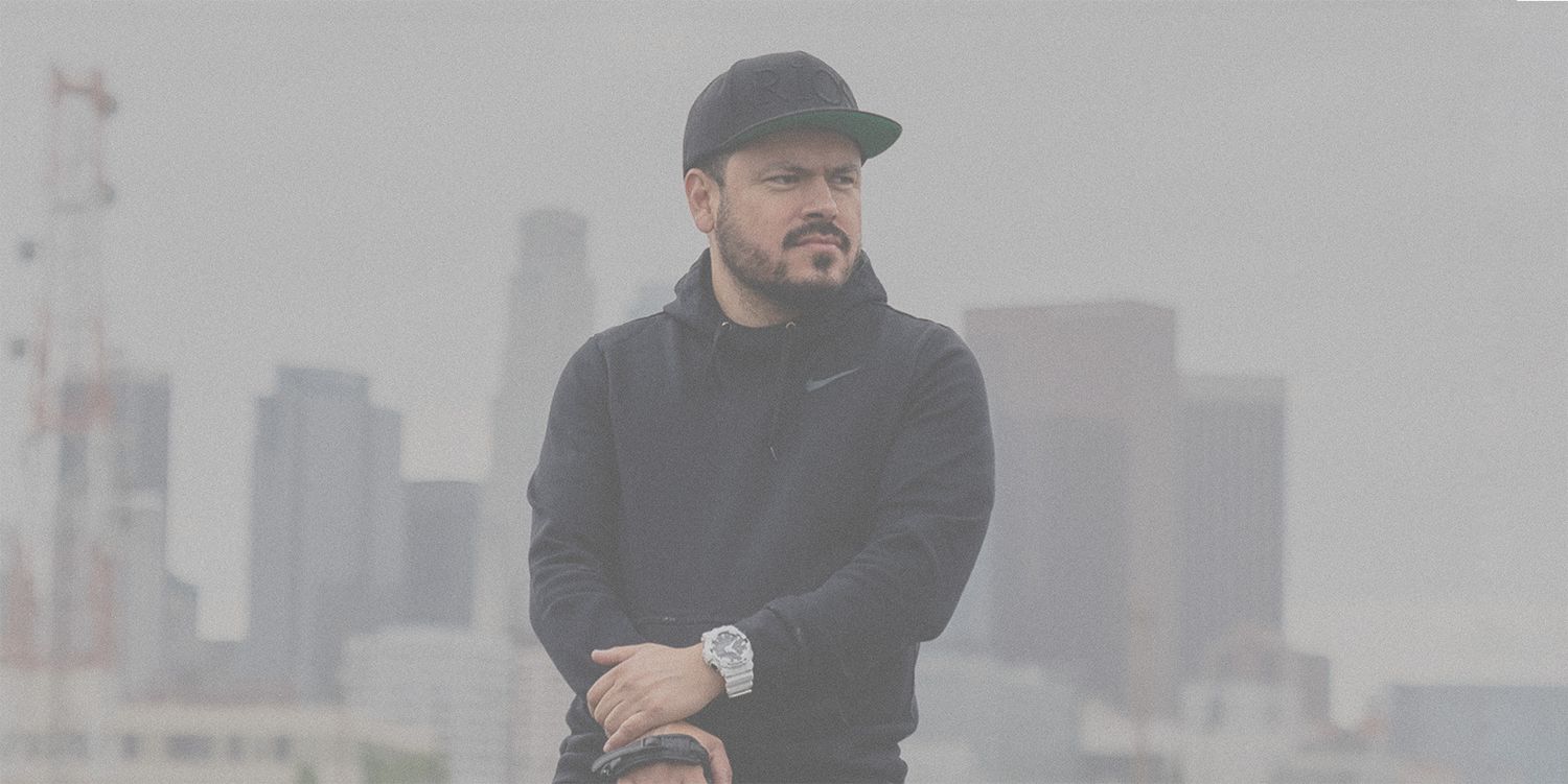 A person in dark clothing stands against a foggy city skyline backdrop.