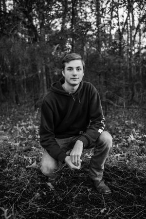 Boy senior crouching down for senior portrait photography. Captured by Maryland Photographer Mallory Bramlett.