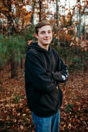 Boy standing with arms crossed in field for senior portrait photography. Captured by Maryland Photographer Mallory Bramlett.