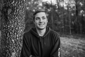 Boy leaning against tree and smiling for senior session photography. Captured by Maryland Photographer Mallory Bramlett.