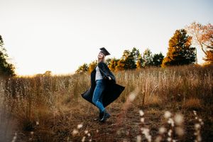 Girl spinning in field in cap and gown for senior portrait photography. Captured by Maryland Photographer Mallory Bramlett.