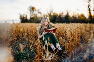 Girl sitting in field with a book for senior portrait photography. Captured by Maryland Photographer Mallory Bramlett.