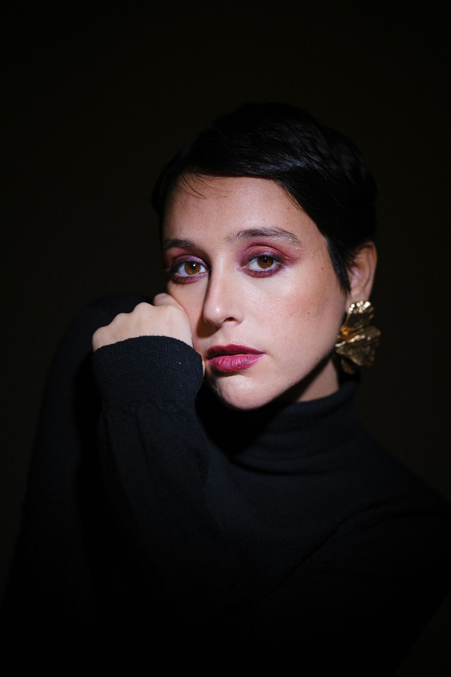 A dramatic close-up portrait showing red lipstick and dark eye makeup against a black background.