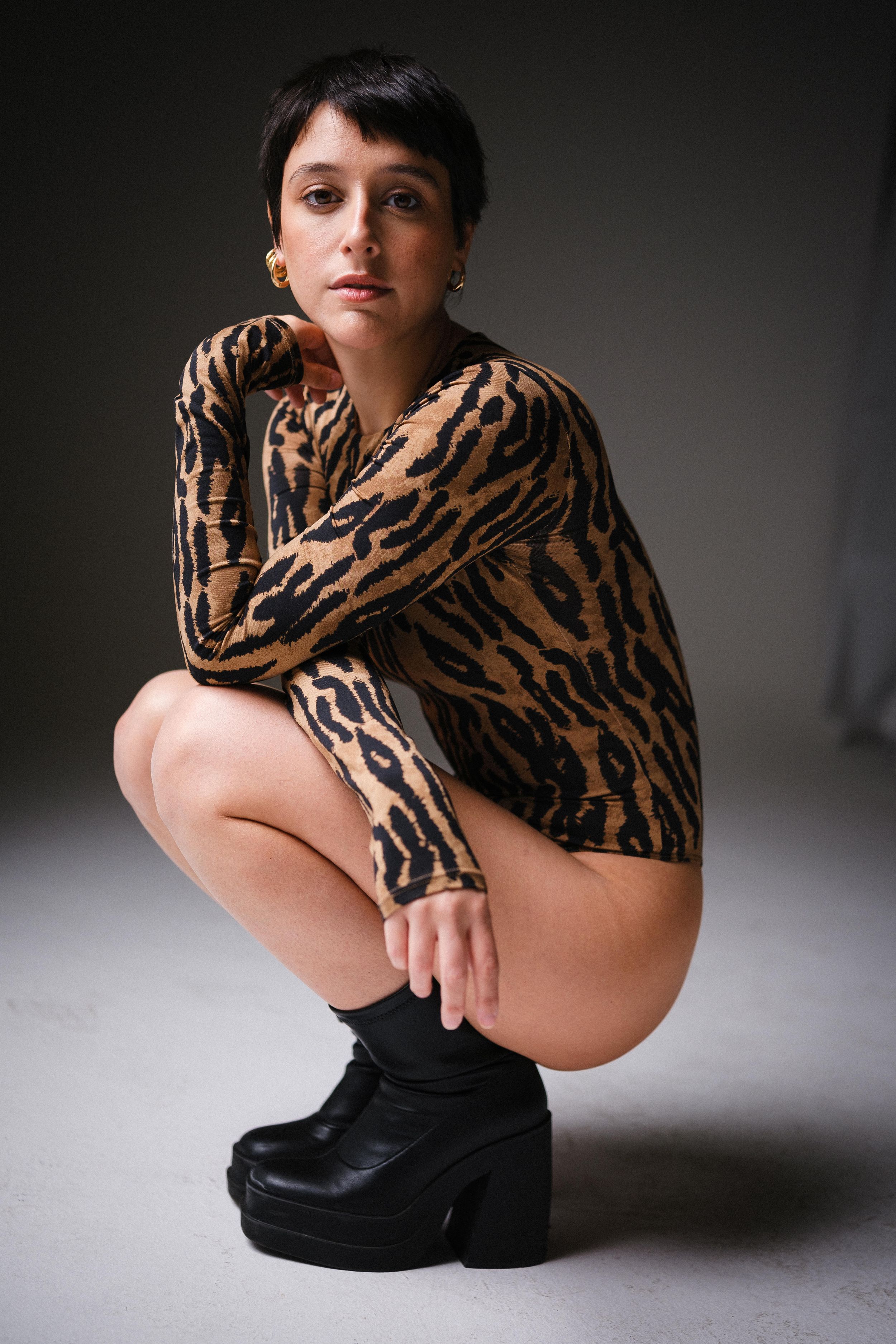 Model in tiger stripe sweater and black boots crouches in dramatic studio lighting.