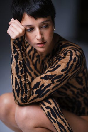 Fashion model wearing tiger print top poses against dark background in artistic photoshoot series.