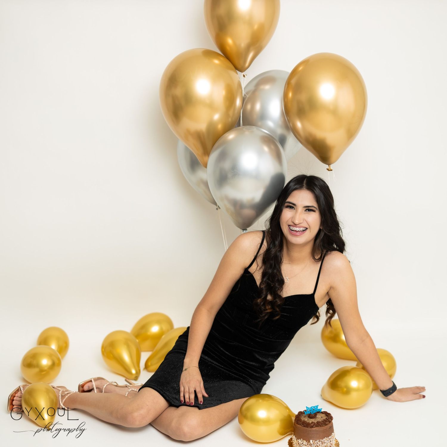 Celebratory portrait with gold and silver balloons and chocolate cake.