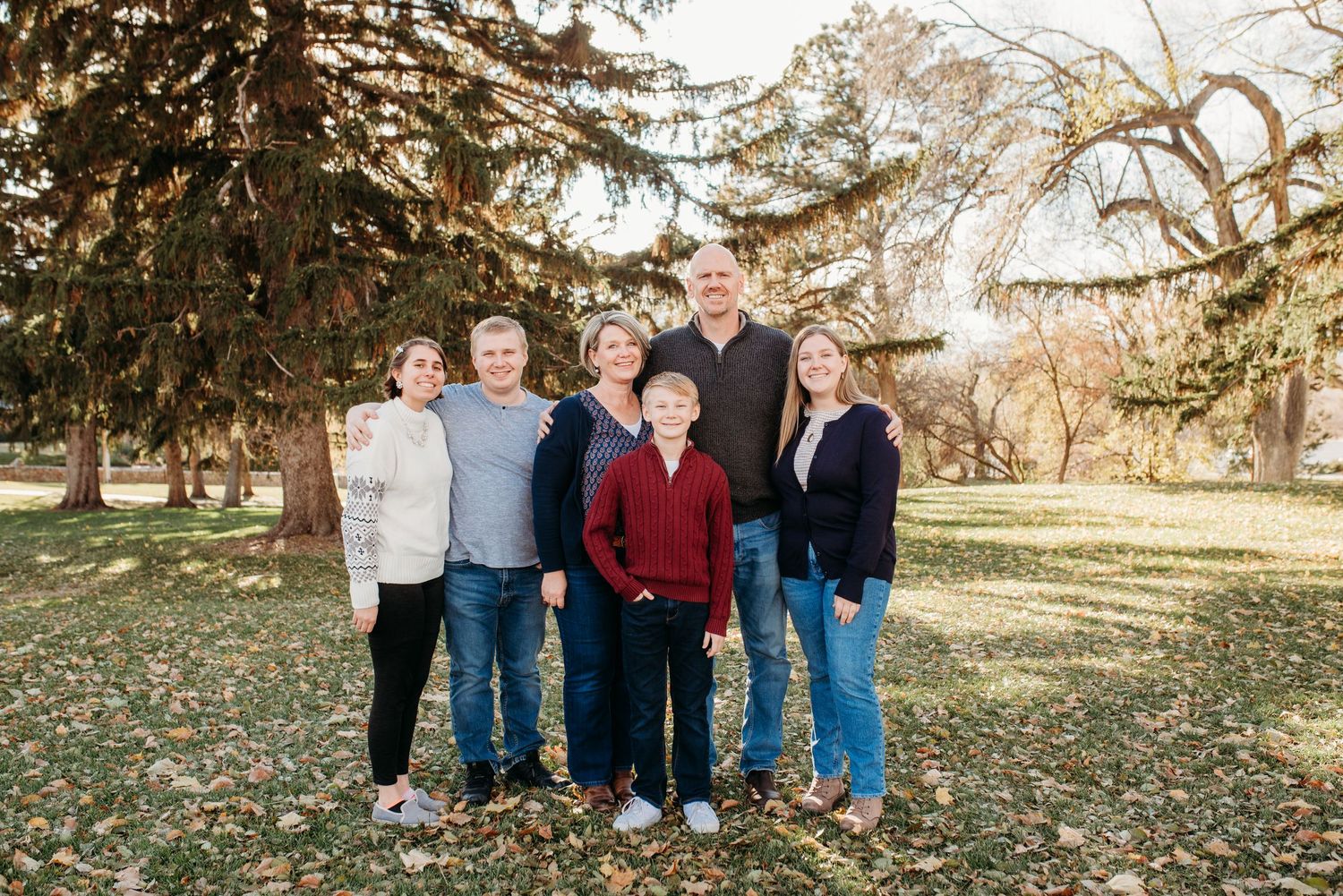 Small group standing together on fallen leaves under evergreen trees.
