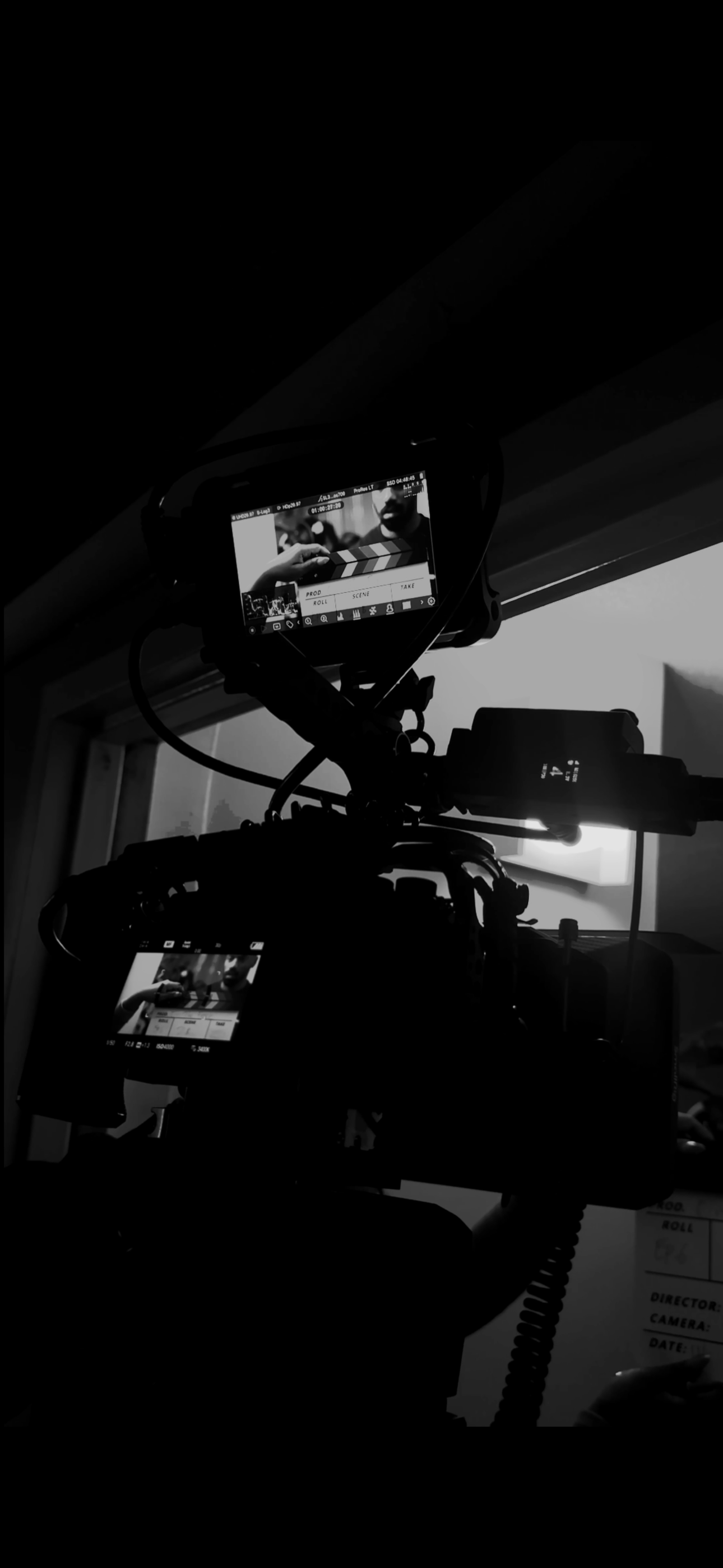 Dark silhouette of professional video camera equipment mounted on a tripod in low light conditions.