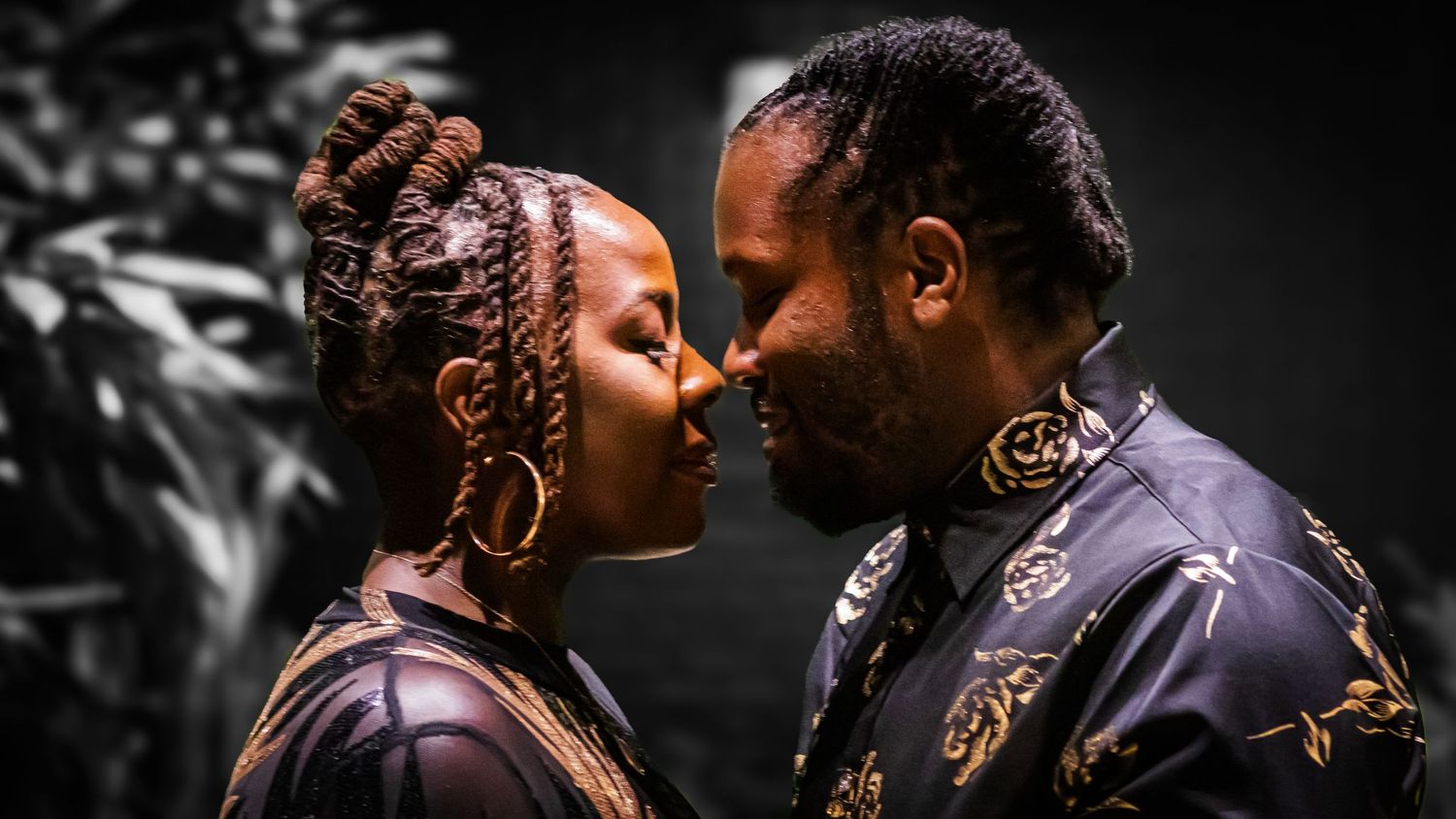 Intimate closeup of a romantic couple in ornate clothing against a dark background.