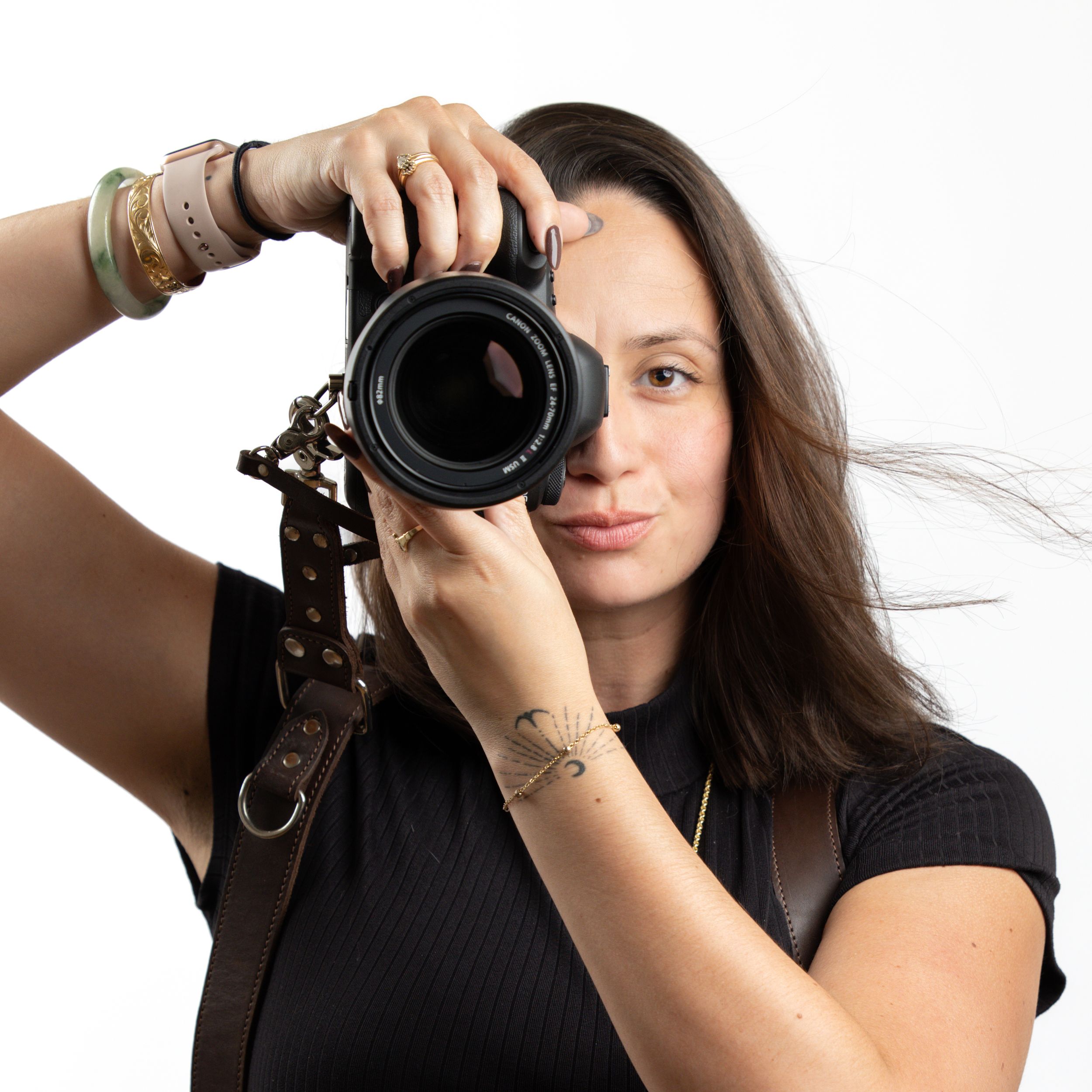 Professional photographer with long dark hair takes photo with DSLR camera against white background.