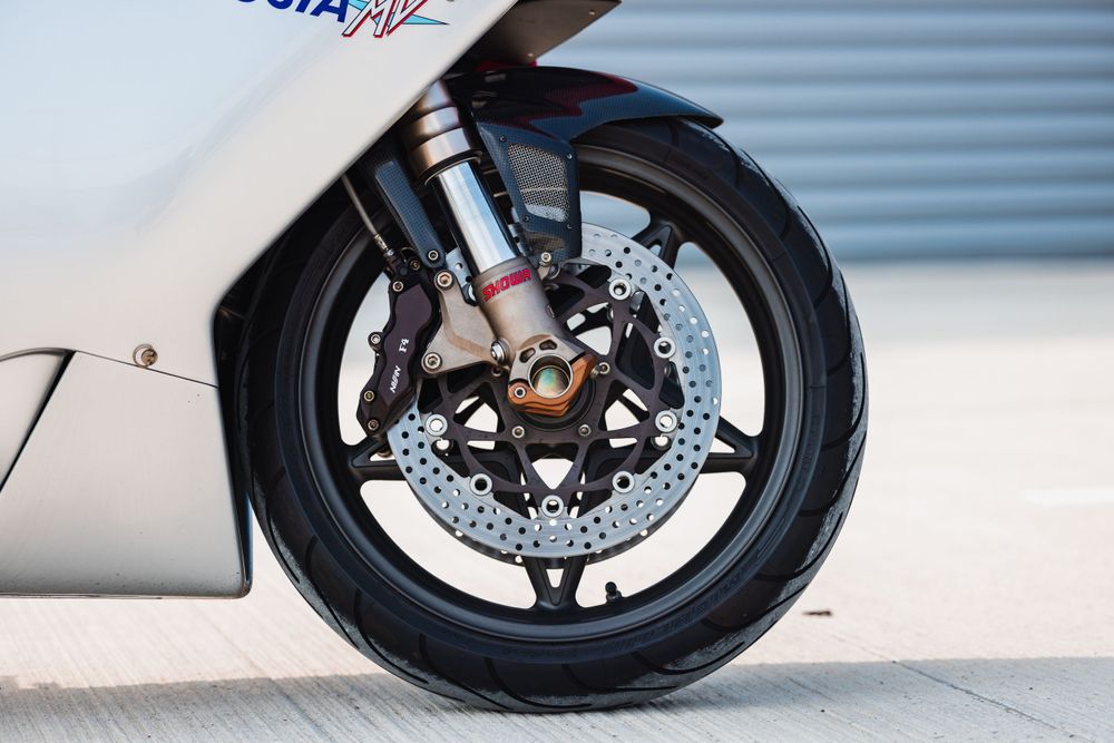 Close-up of a motorcycle front wheel showing disc brake system and black alloy rim against a blurred background.