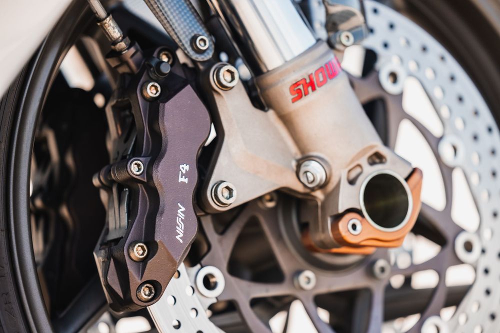 Close-up view of a motorcycle's front brake system showing disc brake, caliper and suspension components in detail.