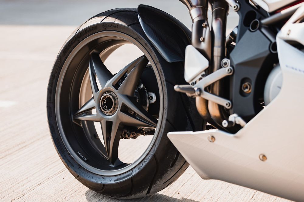 Close-up view of a black alloy wheel and tire on a modern motorcycle parked on concrete pavement.