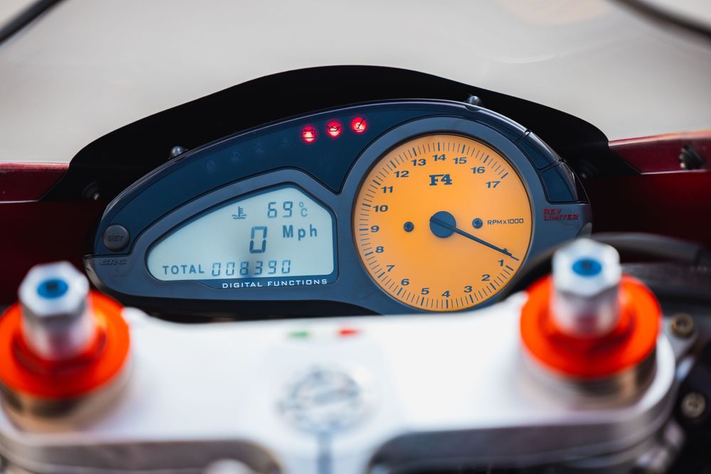 Motorcycle digital dashboard display showing orange tachometer and LCD screen with blue illuminated numbers.
