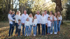 Large multigenerational family posing outdoors in matching white tops and jeans among autumn trees.