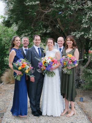 Wedding party poses together outdoors with colorful bouquets featuring bright yellow and pink flowers.