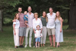 Large family group smiling outdoors on green grass with tall trees in background during summer gathering.