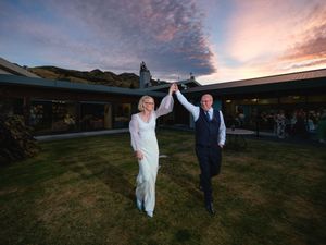 Two people celebrate with raised hands during sunset at an outdoor wedding venue with mountain backdrop.
