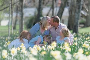 Family sitting in a field of yellow daffodils, parents kissing while children gather around them on a sunny spring day.